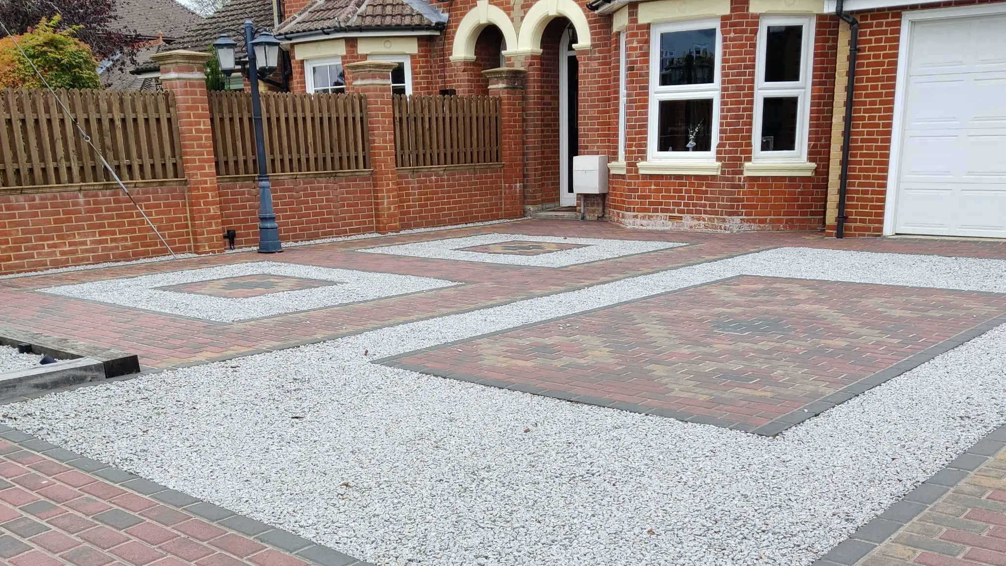 A block paved driveway with gravel inset panels in front of a red brick house